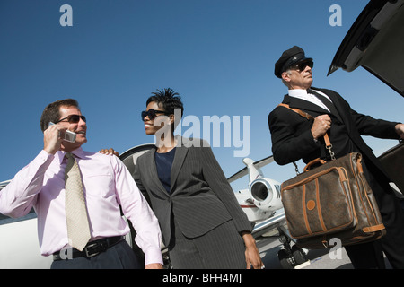 Mid-adult businesswoman, businessman and chauffeur in front of airplane on runway, low angle view. Stock Photo