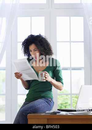 Woman reading paper document, sitting on desk Stock Photo