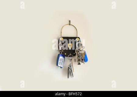 A bunch of keys of all types with key chains hanging on an old wooden key holder nailed on the wall Stock Photo
