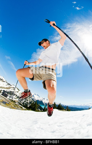A hiker bounds down a summer snowfield above Garibaldi Lake in Garibaldi Provincial Park, BC. Stock Photo