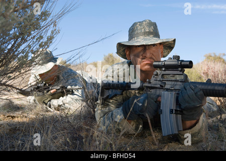 Soldiers aiming rifles in field, focus on soldier in foreground Stock Photo