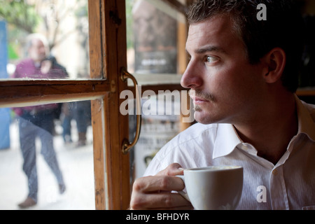 Young man looking out a window and drinking cafe Stock Photo