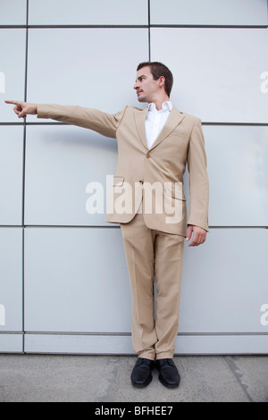 young man in a business suit pointing against a wall Stock Photo