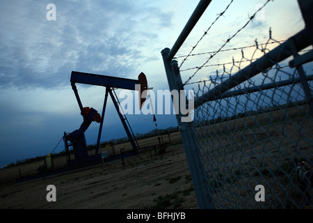 Oil pump jack in evening with fence in Alberta, Canada Stock Photo