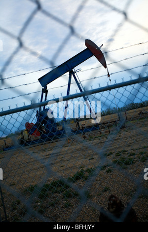 Pump jack behind chain link fence at dusk. Stock Photo