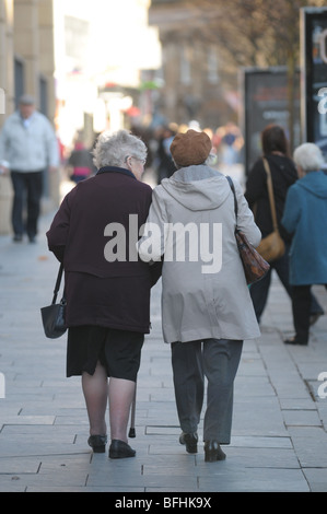 Two elderly ladies holding arms and walking along the pavement. Stock Photo
