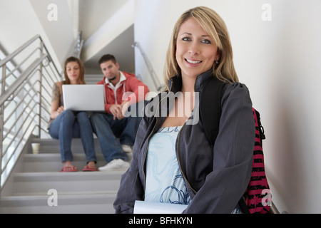 Portrait of female student on stairs, friends using laptop in background Stock Photo
