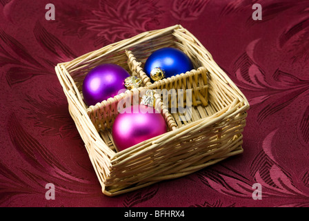 Christmas tree colorful balls arranged in decor basket on purple fabric background Stock Photo