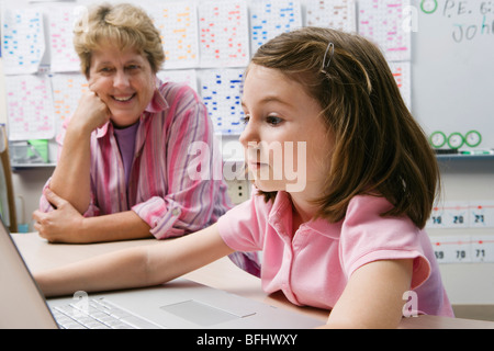 Teacher Watching Schoolgirl Use Laptop Stock Photo