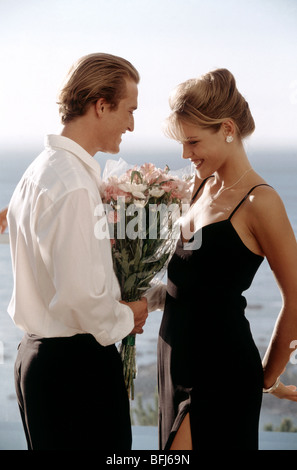 Outdoor seaside image of man presenting flowers to young woman. Stock Photo