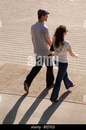 A stylish young couple walk together in the summer sunshine, the sun casting strong shadows behind them. Stock Photo