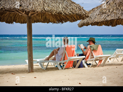 Senior couple relaxing on the beach, man is reading a book and smoking a cigar Stock Photo