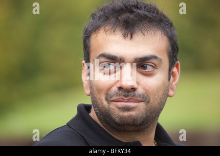 An Asian male with a beard outside looking away from the camera and smiling while playing golf Stock Photo