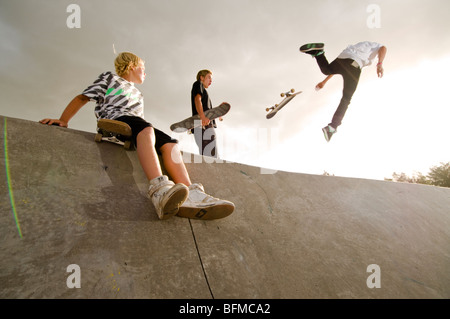3 boys doing tricks in skate park with setting sun, Cambridge, New Zealand, Stock Photo