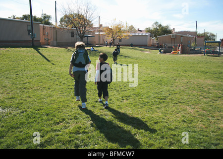 two boys walking together at school on grassy field, elementary school, wearing backpacks Stock Photo