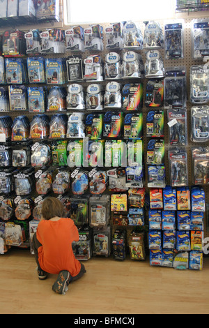 Seven year old boy makes a selection from a large selection of action figure and star wars toys at a toy store, New Mexico, USA Stock Photo