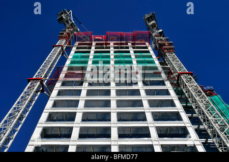 Skywards view up front elevation of new High rise office construction  building site to the current work platforms seen against deep clear blue sky UK Stock Photo