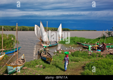 Kenya, Nyanza District. Fishermen return in their boats from fishing in Lake Victoria while women prepare to sell the catch Stock Photo