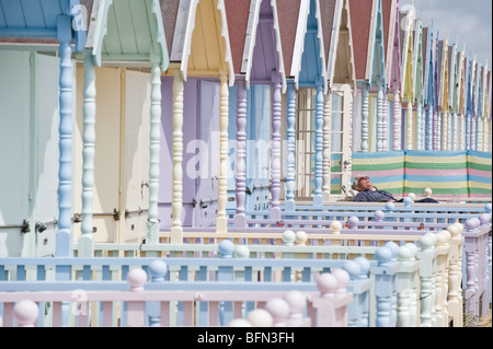 Colourful beach huts on Mersea beach, Mersea Island, Essex. A man relaxes in the sun. Stock Photo