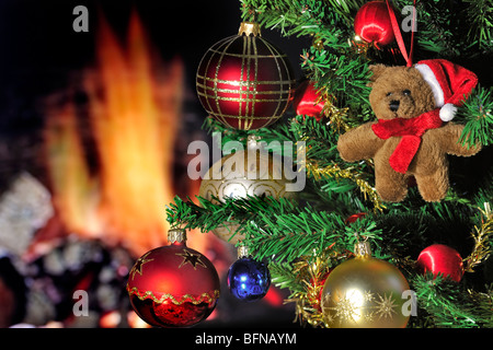 Teddy bear and bells hanging in Christmas tree in front of hearth / fireplace Stock Photo