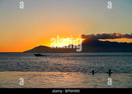People watch sunset while floating in swimming pool at the edge of the ocean at romantic luxury resort in Papeete, Tahiti Stock Photo