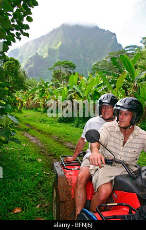 Man and woman ride ATV on jungle adventure down back trails of interior Moorea, Tahiti Stock Photo