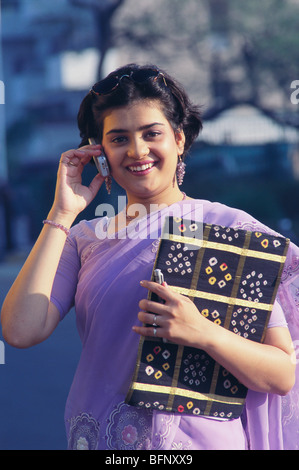 Working lady Indian woman on mobile phone cellphone in violet purple saree sari holding office file India   MR#191 Stock Photo