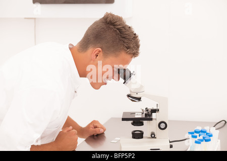 Laboraratory woirk: young smiling researcher looks in microscope Stock Photo