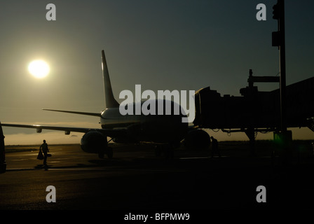 Aircraft stationed at transfer bridge, silhouetted against the early morning sun, Curitiba International Airport, Brazil Stock Photo