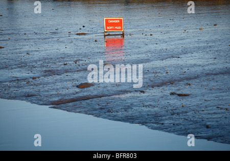 Red sign warning 'DANGER SOFT MUD' standing in an expanse of soft mud. Stock Photo