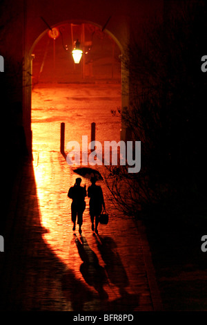 Couple walking in the rain are silhouetted under the Drosdy Arch Stock Photo