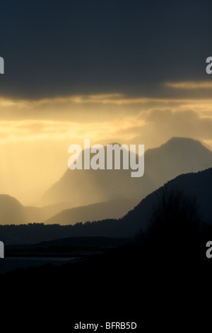 Sun penetrating dark clouds in mountainous landscape in Norwegian fjord Stock Photo