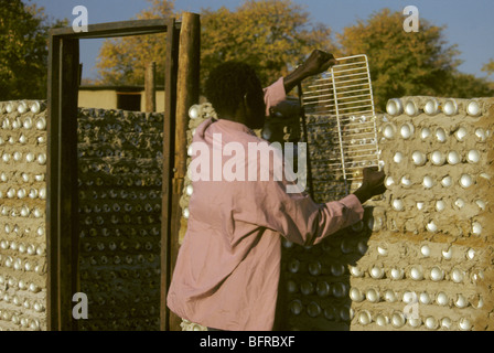 Man building a mud wall using empty tin cans Stock Photo