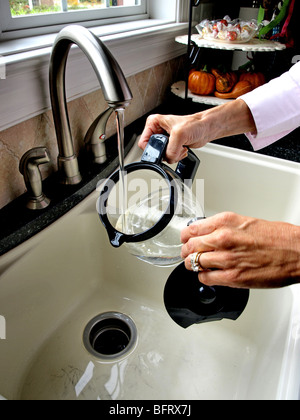 woman putting water into coffee carafe pitcher from faucet in sink in kitchen close-up Stock Photo