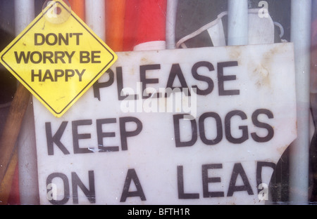 View from outside through window with parasols leaning against it and signs Please keep dogs on lead and Dont worry be happy Stock Photo