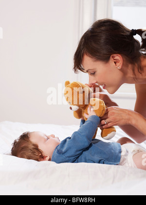 baby playing teddy bear laying on yellow bed Stock Photo - Alamy
