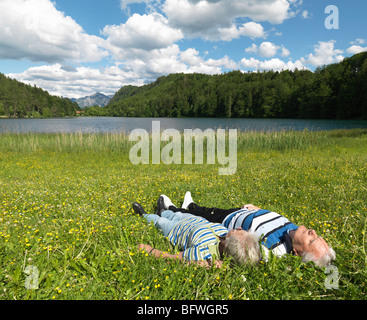 Senior couple lying in field by lake Stock Photo