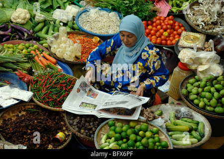 Malay or Malaysian Woman Reading Daily Newspaper on Vegetable Market Stall, Central Market, Kota Bahru, Malaysia Stock Photo