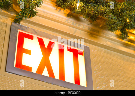A closeup of an exit sign, lit, with green garland and white Christmas lights beside. Stock Photo