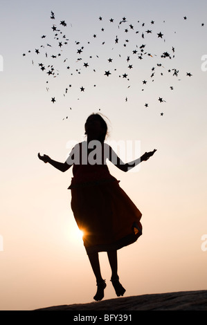 Silhouette of a young Indian girl jumping and throwing stars at sunset. India Stock Photo