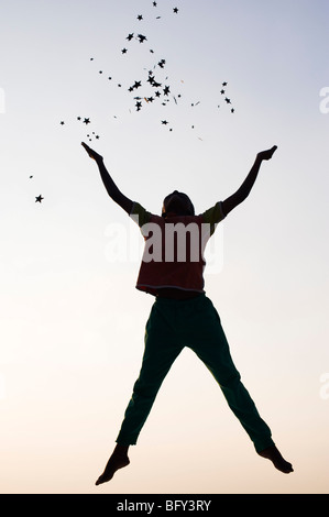 Silhouette of a young Indian boy jumping and throwing stars at sunset. India Stock Photo