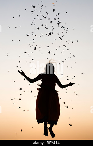 Silhouette of a young Indian girl jumping and throwing stars at sunset. India Stock Photo