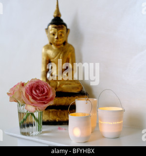 Golden Buddha statue, pink roses and candles on a shelf Stock Photo