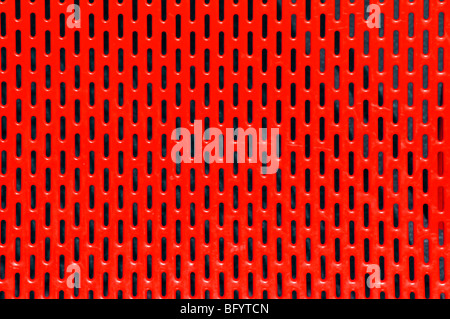 Close up bright red painted strong sheet steel panel with regular spaced repetitive equally spaced ventilation slots as an abstract pattern picture Stock Photo
