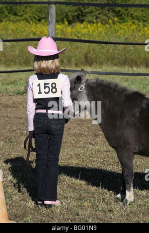 Young girl with pink boots and cowboy hat competing in a horse show halter class with a fuzzy gray miniature horse.. Stock Photo