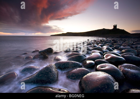 Dawn over Embleton Bay, basalt boulders in foreground and ruins of Dunstanburgh Castle in background, Northumberland, England Stock Photo