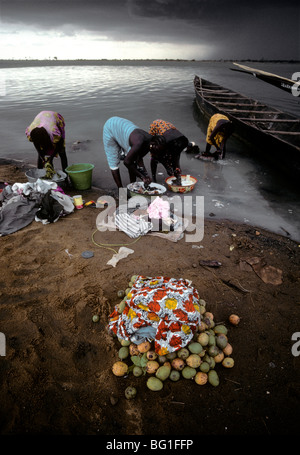 Women wash clothes in the Niger River at Segou, Mali, West Africa. They have unloaded mangoes from a pirogue and await a vendor to pick them up. Stock Photo