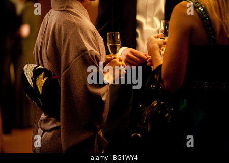 Japanese woman in kimono drinking champagne with Woman in Western style dress, and man in black tie.. Stock Photo