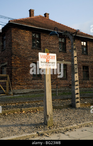 Perimeter electric fence & warning sign at Auschwitz Nazi death camp. Oswiecim, Poland. Prisoner accommodation block is behind. Stock Photo