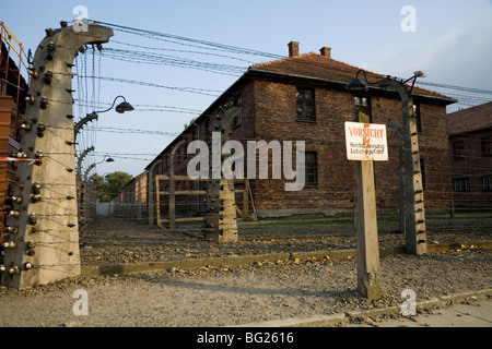 Perimeter electric fence & warning sign at Auschwitz Nazi death camp. Oswiecim, Poland. Prisoner accommodation blocks are behind Stock Photo